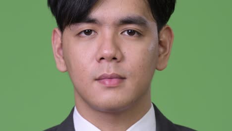 young handsome asian businessman against green background