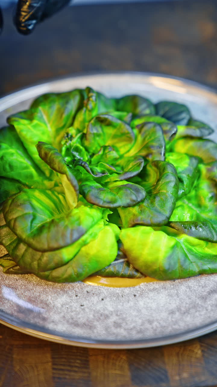 Leaves of green salad are on the plate. Hands in black latex gloves put some pieces of fish. Close up. Vertical video.