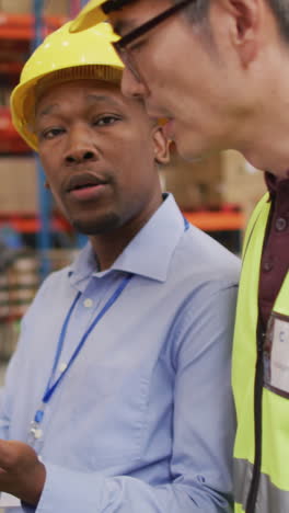 diverse male workers wearing safety suits and talking in warehouse