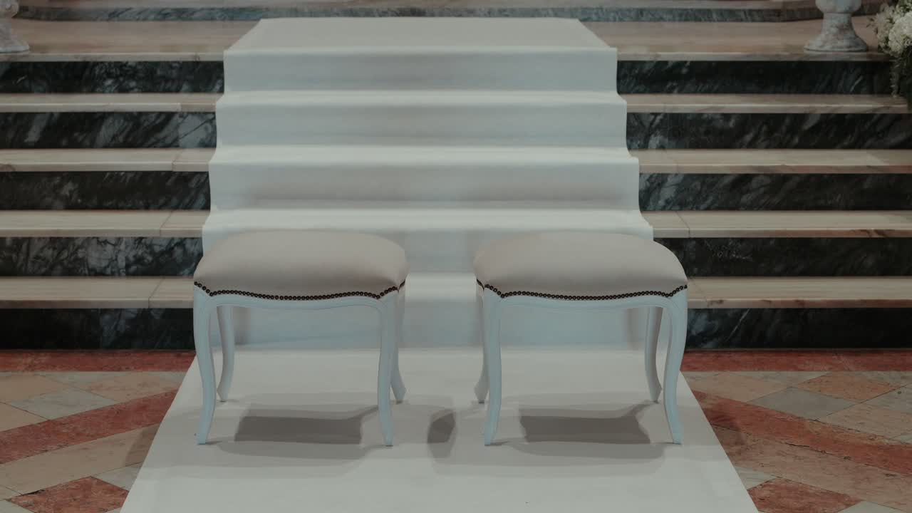 taburetes para ceremonias de boda colocados en un pasillo blanco frente a unas escaleras de mármol