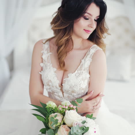 video shot of a young bride in a wedding dress on the background of a bed. attractive model with modern hairstyle in white dress is posing to camera inside the light room.