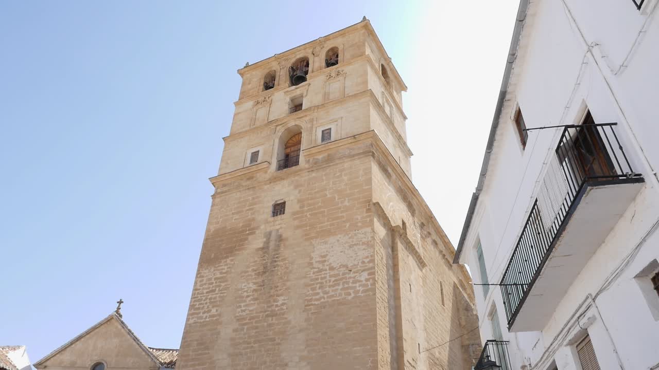 Vista dal basso del campanile rinascimentale della Chiesa dell'Incarnazione ad Alhama de Granada. Luce naturale, cielo azzurro limpido, architettura tradizionale andalusa.