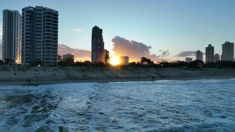 drone shot low over ocean, flying backwards with waves and sun reflecting off water