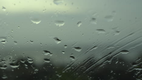 Closeup-of-water-droplets-trickling-down-on-wet-clear-car-window-glass-during-heavy-rain-against-beach-view-in-rainy-day-monsoon-season