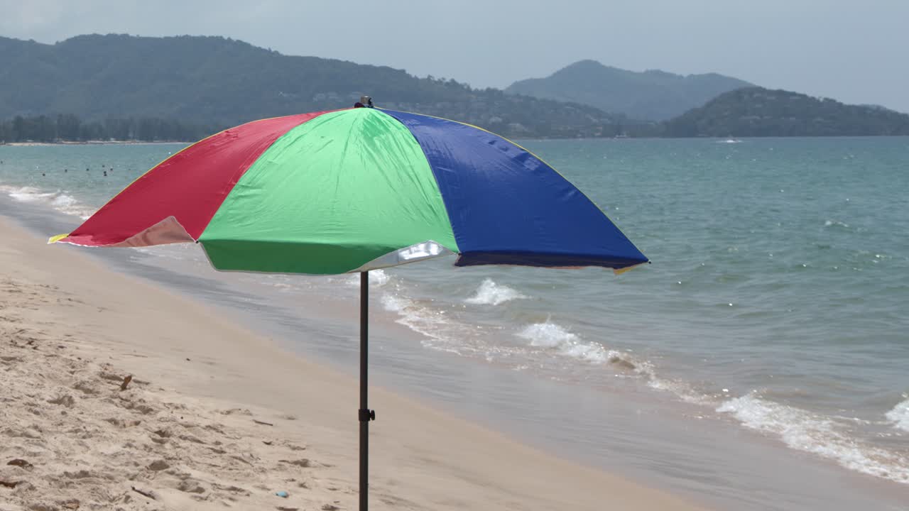 Un plan large fixe d'un parasol multicolore sur une plage de sable avec des vagues océaniques