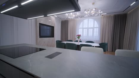 spacious open-plan kitchen with marble island and dining area, featuring modern lighting fixtures, herringbone wood flooring, and teal accent chairs