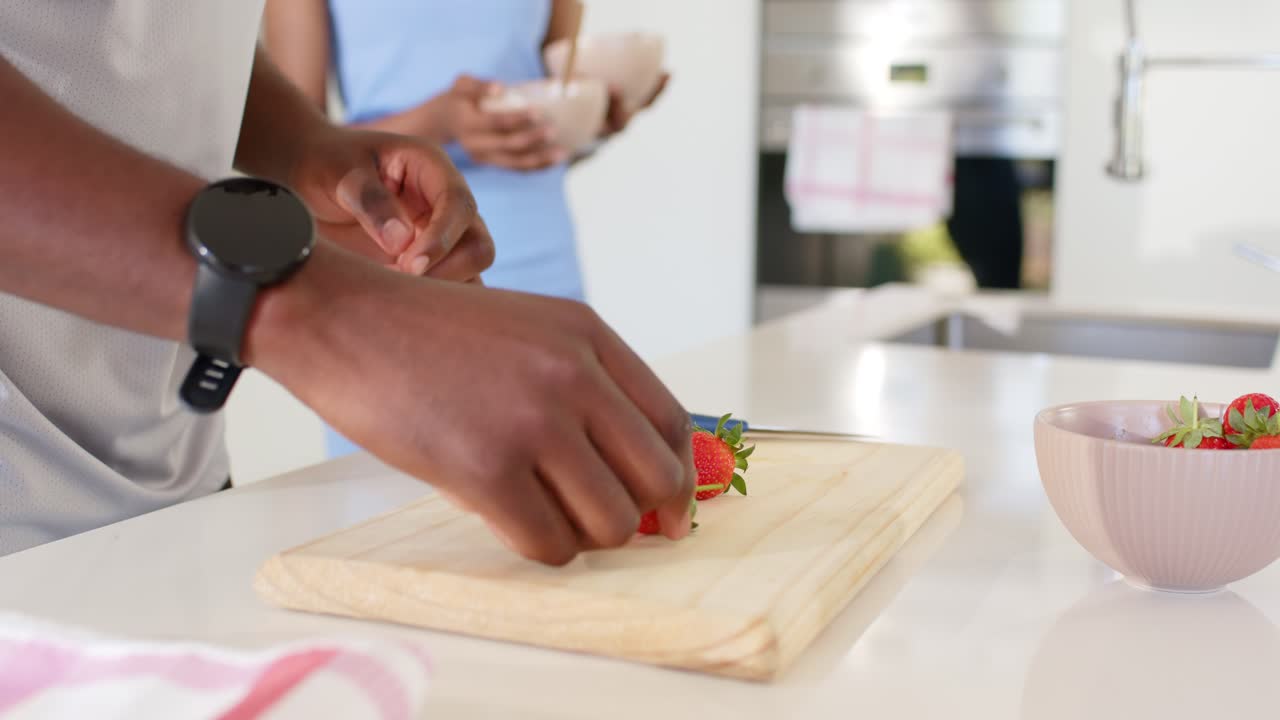 Hands are trimming strawberries on board after placing strawberry as partner sets bowls for serving
