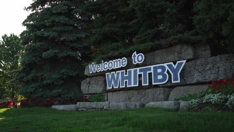 welcome to whitby canada sign with sunshine glaring through the trees in a botanical garden setting with low panning shot