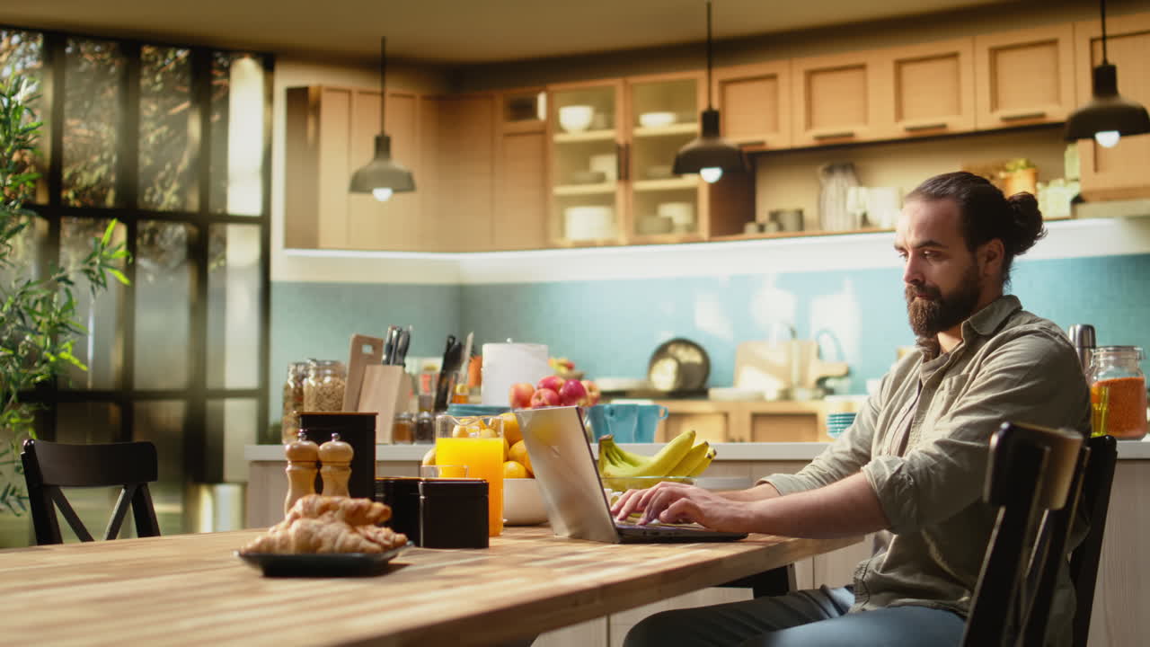 Homem trabalhando em casa com o notebook na mesa da cozinha