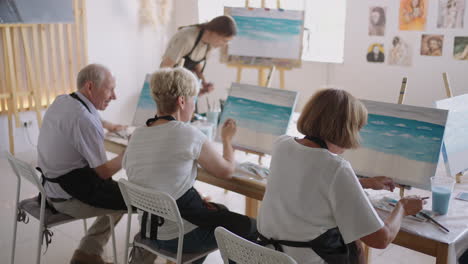 slow motion old people attend drawing courses. the teacher helps pensioners who attend drawing courses to draw. a group of retired friends at a drawing lesson