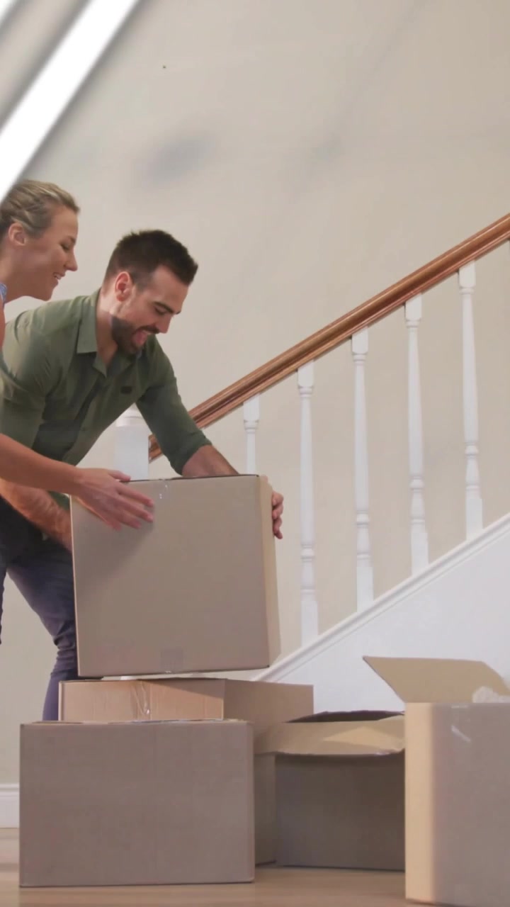 Vertical video: Man with box reaching stack, woman helping stack boxes for move, charts sweeping