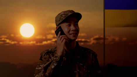 soldado hablando por teléfono durante el atardecer con la bandera ucraniana en el fondo