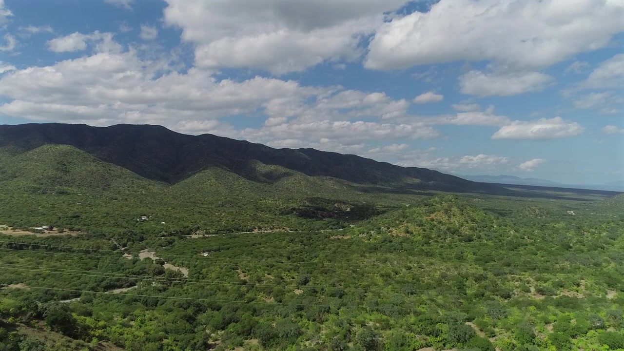 Vista aerea 4K con drone che si alza e avanza sopra verdi colline desertiche vicino a La Ventana, con nuvole a cumulo e le loro ombre che fluttuano sopra