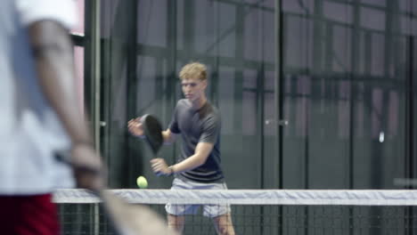young man playing padel tennis, preparing to serve on indoor court