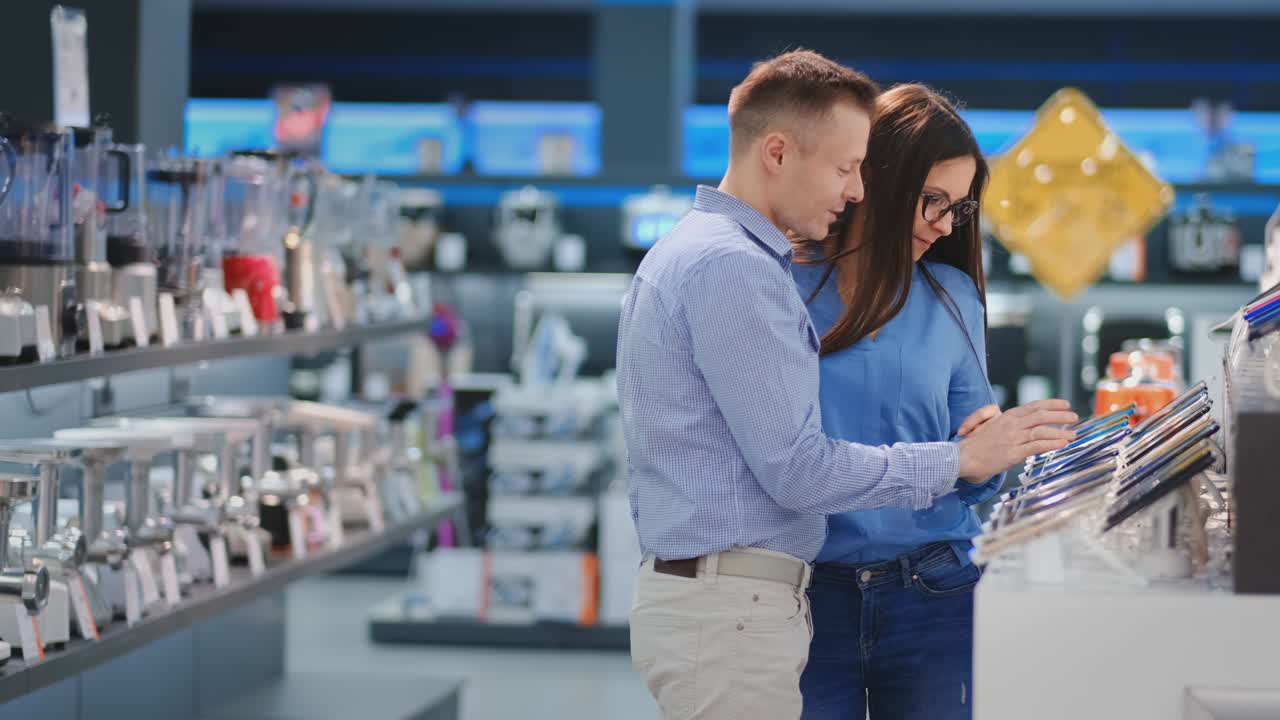pareja feliz hombre y mujer de pie en el mostrador con teléfonos móviles en ropa casual eligiendo un nuevo teléfono inteligente en una tienda de electrónica moderna