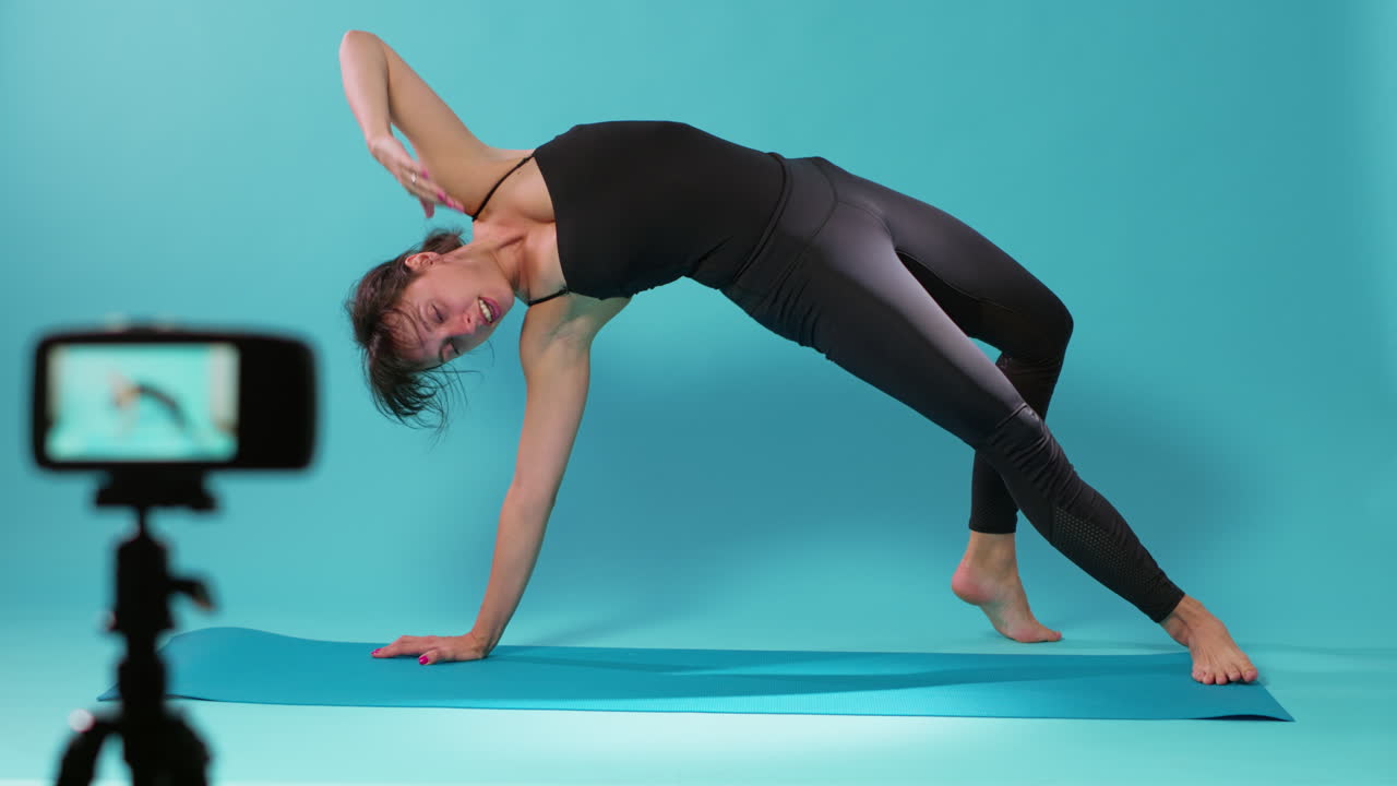 Yoga instructor filming stretching exercise on camera in studio