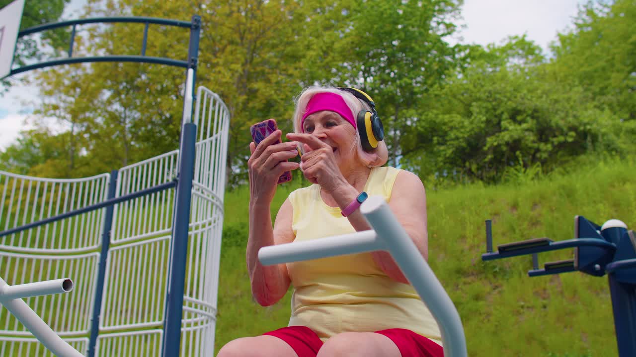 mujer mayor después del entrenamiento deportivo escuchando música en el patio de recreo, celebrando la victoria haciendo el gesto del ganador