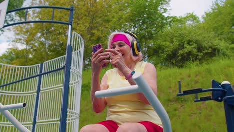 Mujer-Mayor-Después-Del-Entrenamiento-Deportivo-Escuchando-Música-En-El-Patio-De-Recreo,-Celebra-La-Victoria-Haciendo-Un-Gesto-De-Ganador