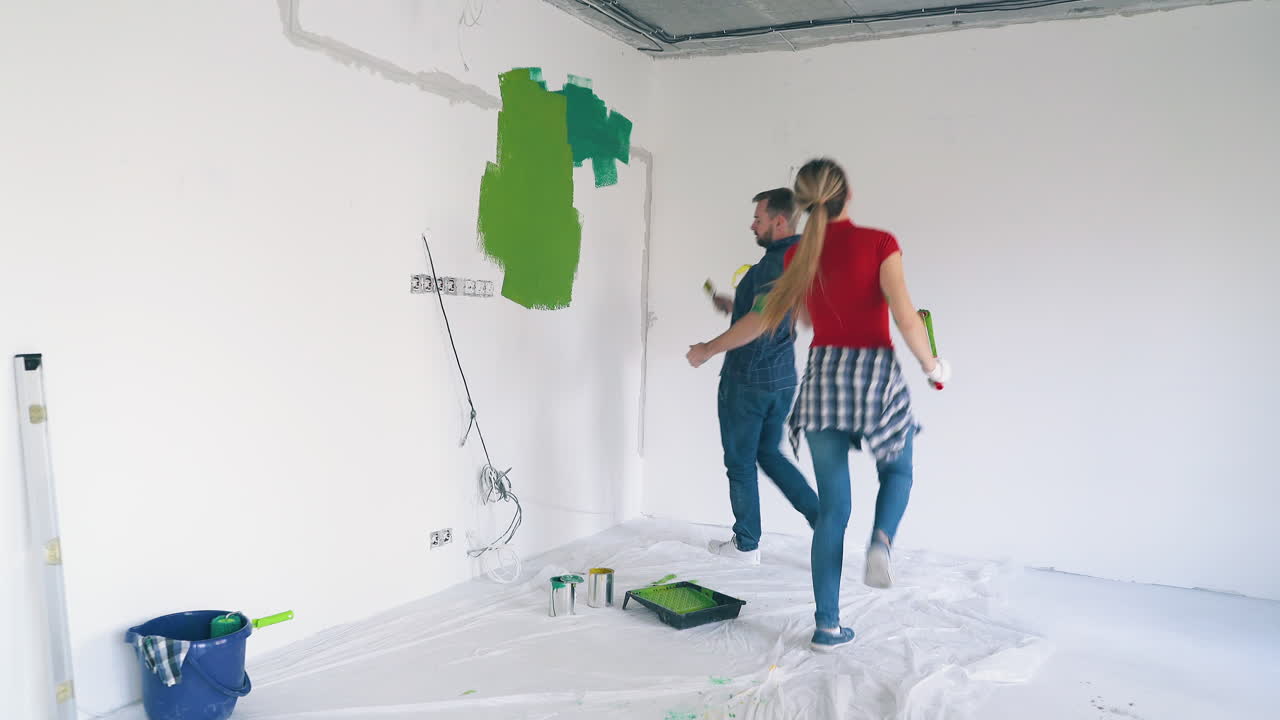 la pareja se divierte pintando la pared blanca en la habitación de renovación