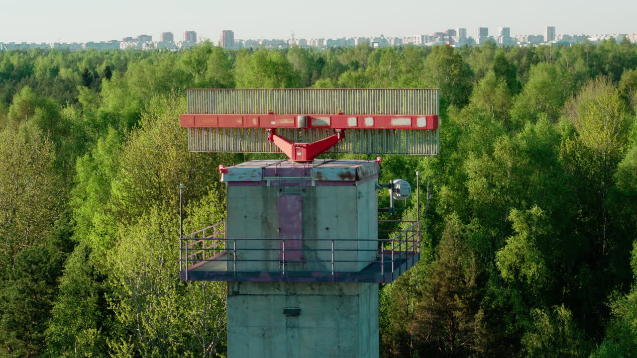 Old and worn secondary surveillance radar for air traffic control rotating in the middle of forest with city visible in background