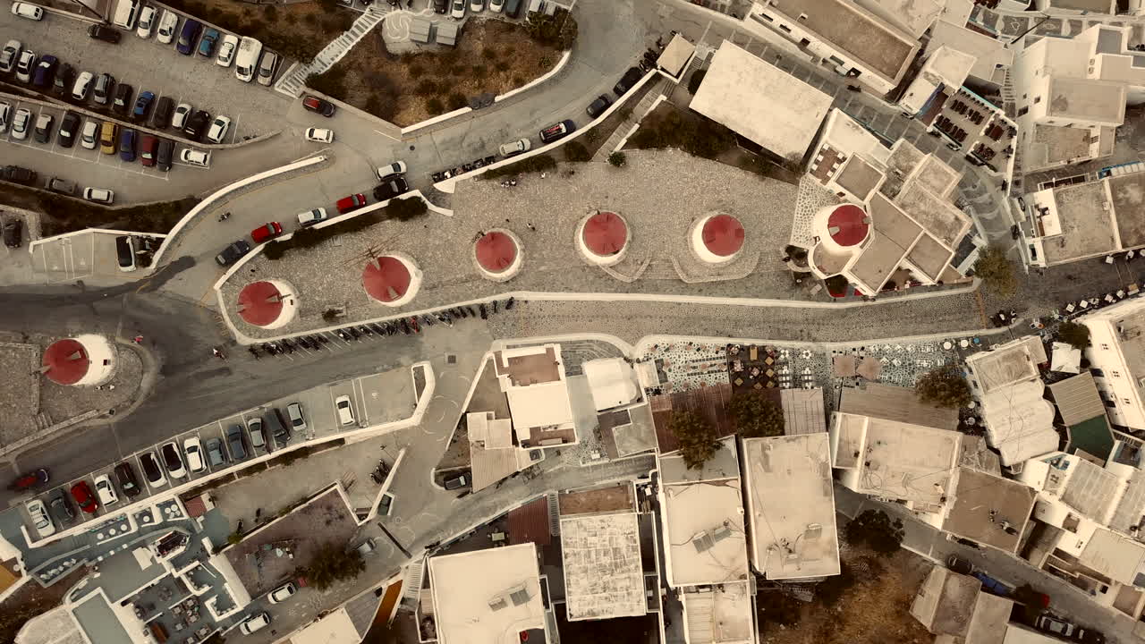 Greece, Astypalea Island's famous wind mills on a drone footage during sunset. traffic down below and the car parking at the old town. Flat white house roof tops and red circular wind mill roofs.