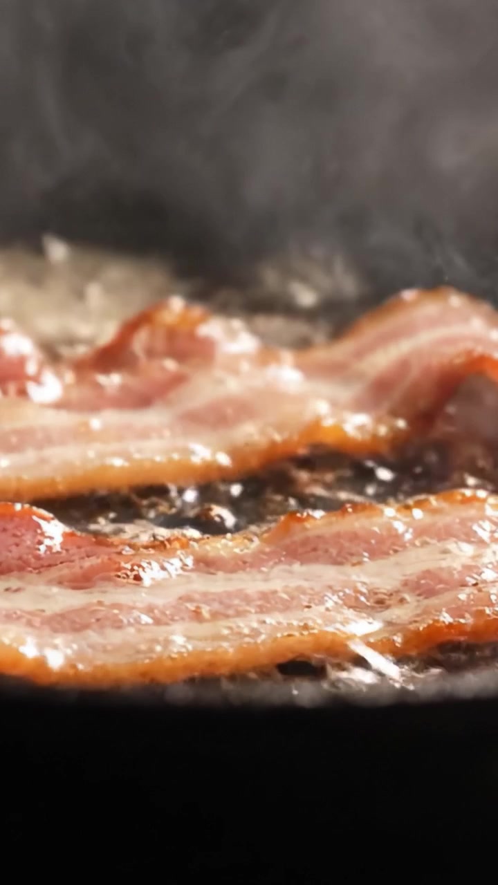 Spruttende bacon, der steges på panden: En lækker kulinarisk oplevelse med sprøde strimler tilberedt i herligt fedt, perfekt sprødstegt til morgenmadselskere overalt.