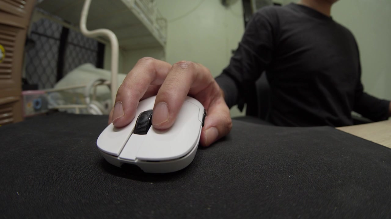 Person using a white computer mouse on a desk in a home office environment