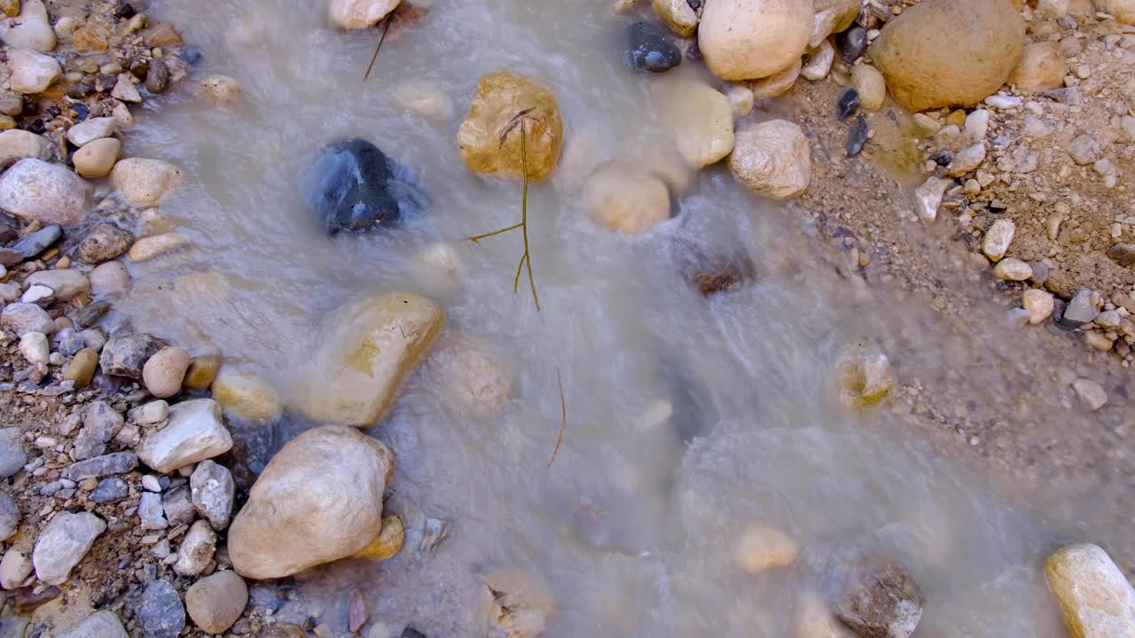 corriente de agua dulce turbia con agua arenosa que fluye sobre arena, guijarros y rocas en un entorno natural al aire libre de naturaleza salvaje