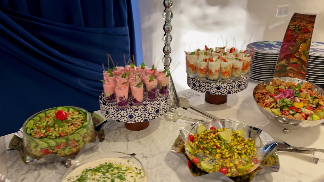 Buffet catering per eventi al coperto con insalate assortite, salse cremose e coppe di dessert colorate disposte su un tavolo di marmo sotto una morbida illuminazione dell'ambiente