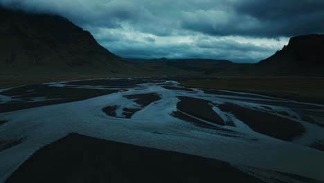 drone aéreo de un río serpenteante retorcido en la fría oscuridad de las nubes ominosas y la cordillera montañosa