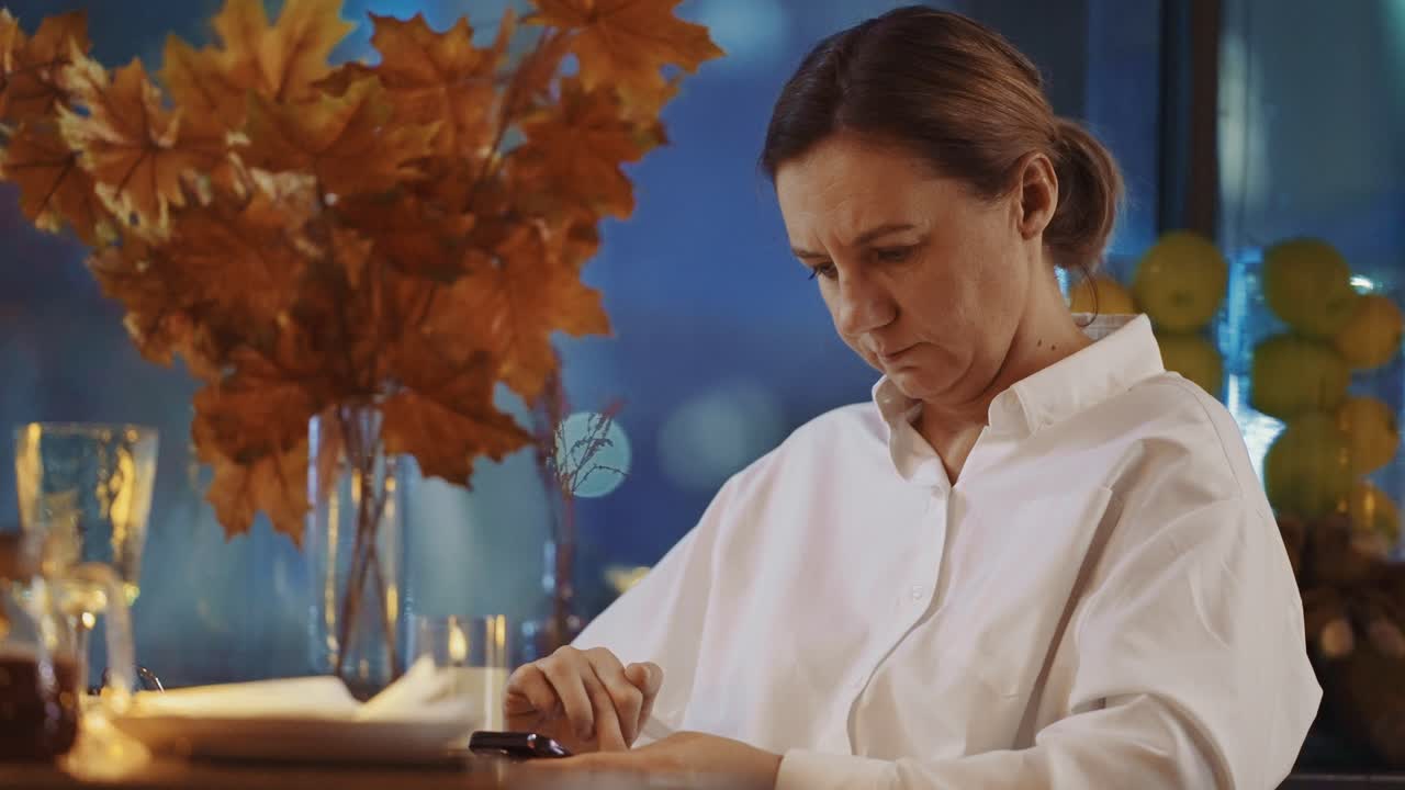 Tankefuld kvinde bruger smartphone på en aften-café