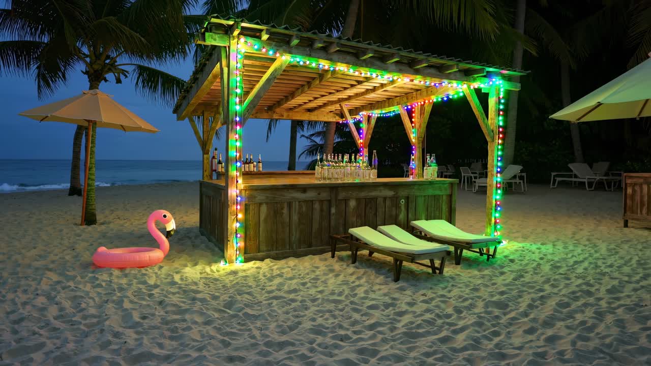 Beach bar decorated with colorful string lights sets a festive mood on a tropical beach at night, with lounge chairs inviting guests to relax and enjoy the ambiance