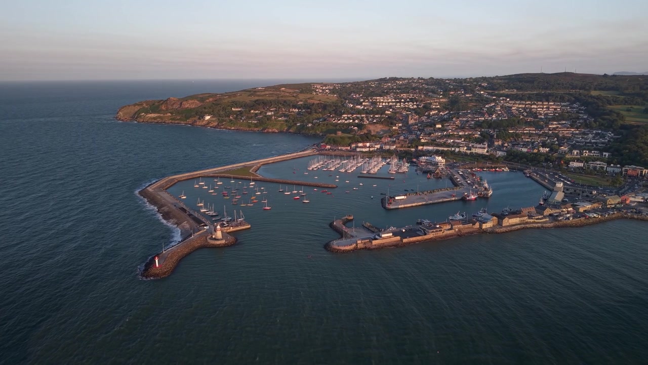 İrlanda'da, Altın Rengi Akşam Işığında Parlayan Howth Limanı ve Sahil Kasabasının Destansı Geniş Açılı Havadan Görünümü