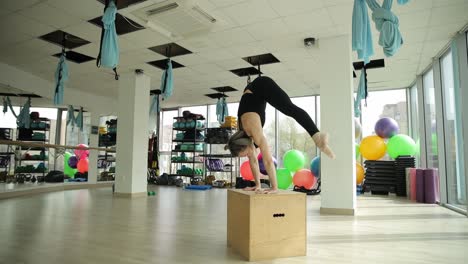 woman performing handstand on a box in a fitness center