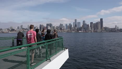 group of tourists enjoying the view of seattle's skyline, including the space needle, from the deck of a ferry on a sunny day.