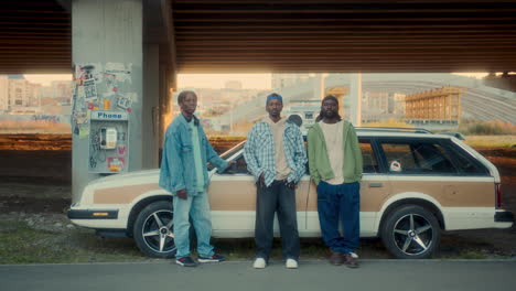 group of black friends posing by vintage car with cityscape in background