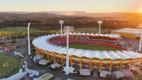 drone captures a sweeping aerial view of a large sports stadium at sunset, highlighting dramatic lighting, modern architecture, and surrounding landscape in gold coast, australia