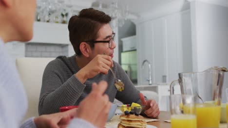 padres asiáticos felices en la cocina comiendo el desayuno y hablando con la hija sonriente