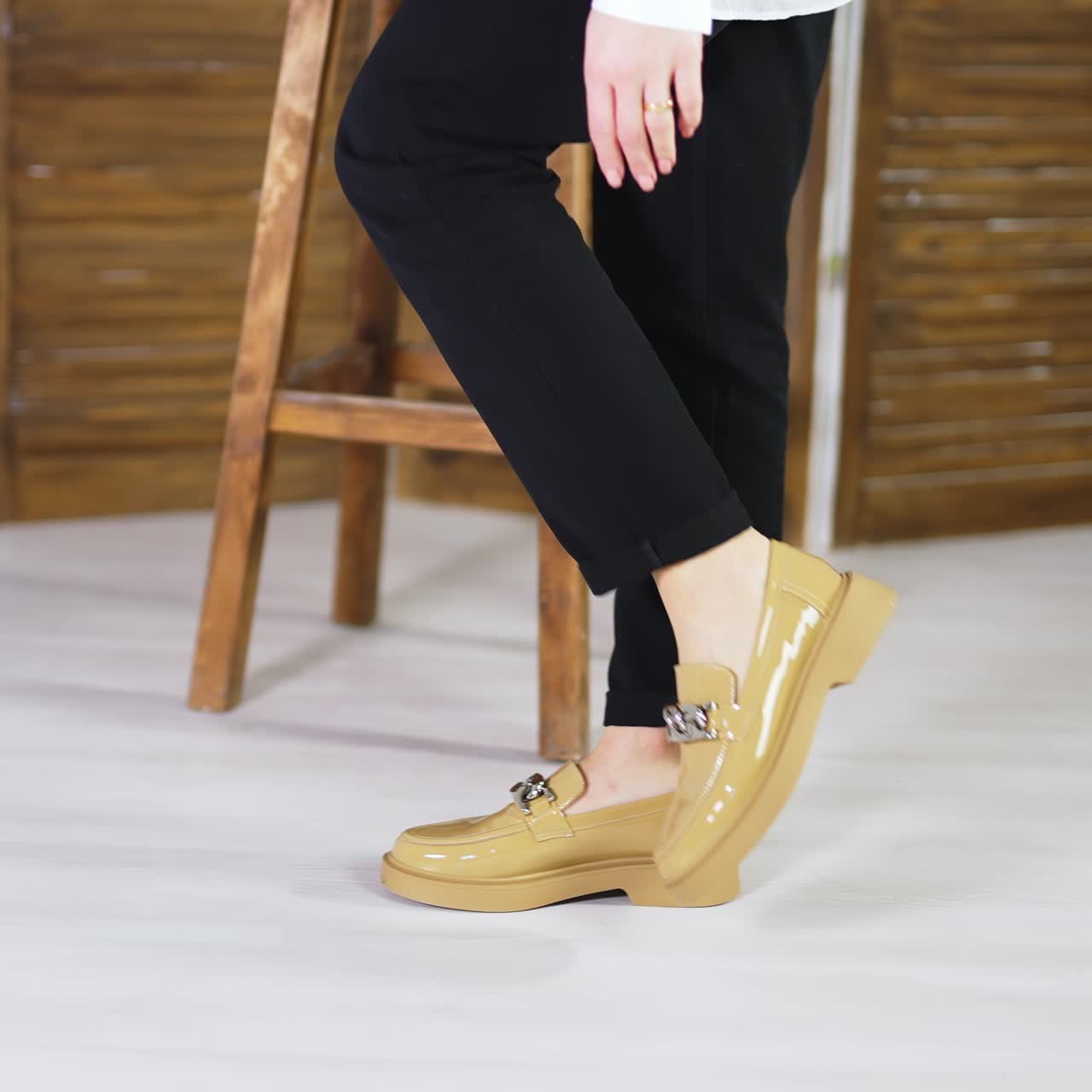 Female walking back and forth in fashionable new shoes. Beige stylish footwear on plain soles with chain decoration. Wooden stool and folding screen at backdrop