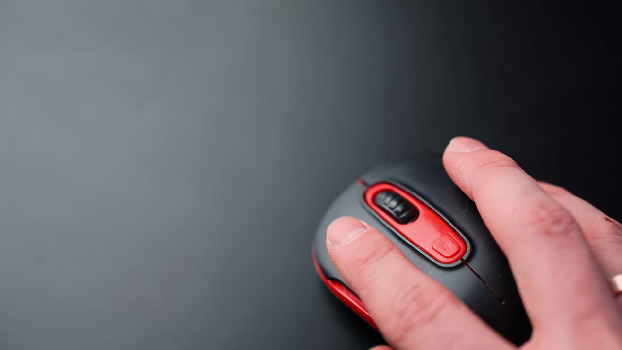 Top-down view of a hand using a black and red wireless mouse on a clean dark desk with large copy space, ideal for office workflow, browsing, and tech productivity b-roll