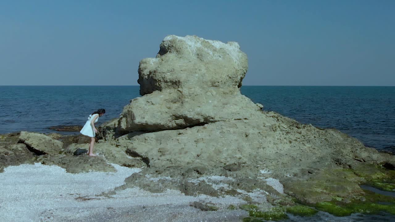 해변에서 하얀 드레스를 입은 예쁜 소녀의 공중 슬로우 모션 샷