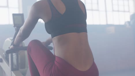 vista trasera de una mujer afroamericana entrenando en una máquina de remo en el gimnasio, en cámara lenta.