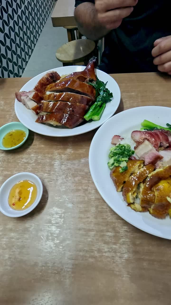 Tangan menyajikan paha angsa panggang (si yip) dengan sepiring ayam panggang (Siu Gai) dan perut babi renyah (Siu Yuk) di restoran lokal. Menikmati makanan Kanton tradisional otentik di Hong Kong.