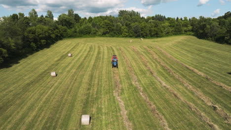 Campo-Verde-Con-Tractor-Y-Fardos-De-Heno-En-Oronoco,-Minnesota,-EE.UU.---Retroceso-Aéreo