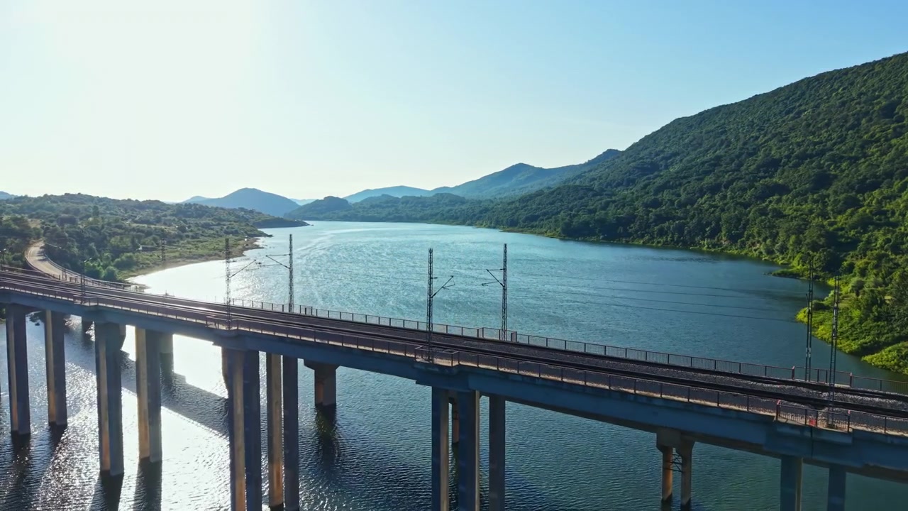 丘陵地帯の晴れた日、高い橋の近くの水面に太陽の光が反射している。