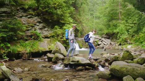 a young couple of tourists with backpacks crosses a mountain river in the forest hd video