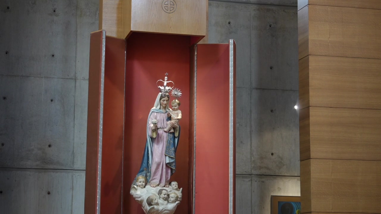 Statue of Virgin Mary holding child displayed in church niche with red background and modern wall panels in religious interior