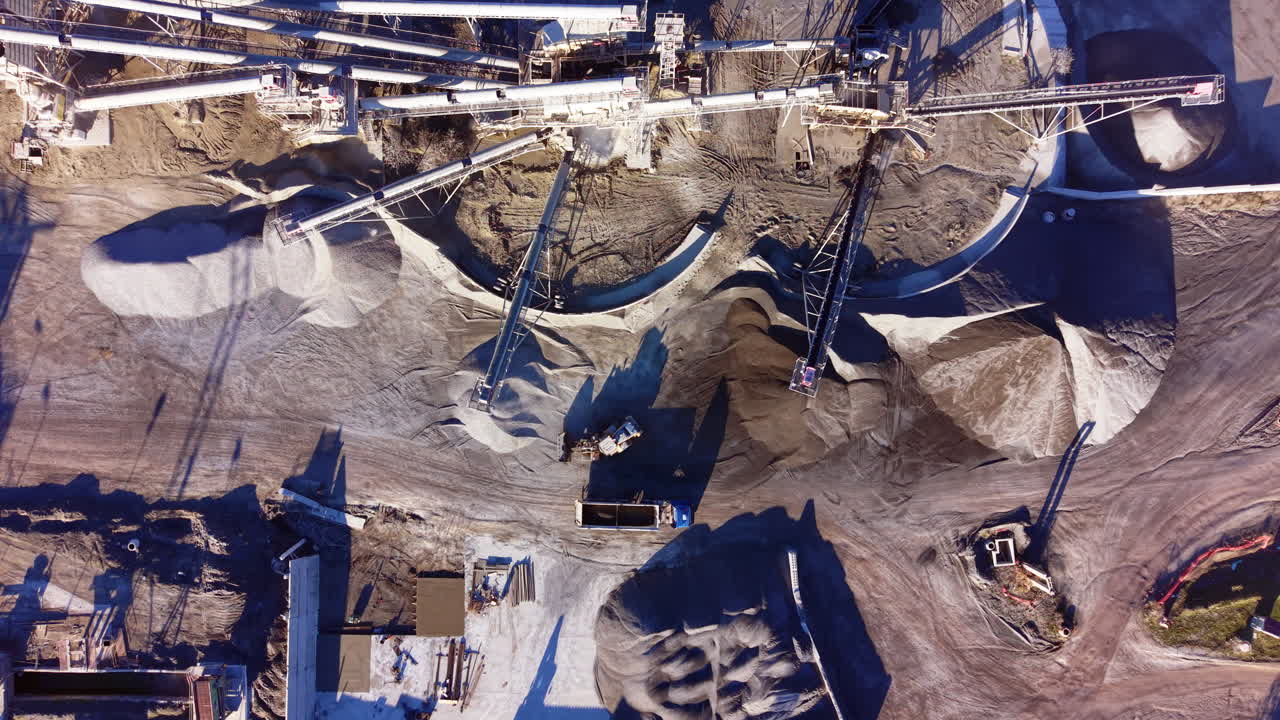 Industrial arrangement of conveyor systems and organized piles of processed stone at a mine. Top down aerial view of quarry conveyor belts and stockpiles