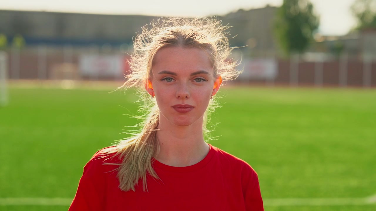 Jonge sportvrouw staand op een voetbalveld bij zonsondergang