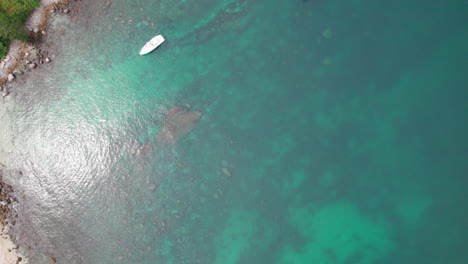 aerial drone footage with a top-down view of turquoise sea, boats, and clear water revealing the seabed by a rocky beach